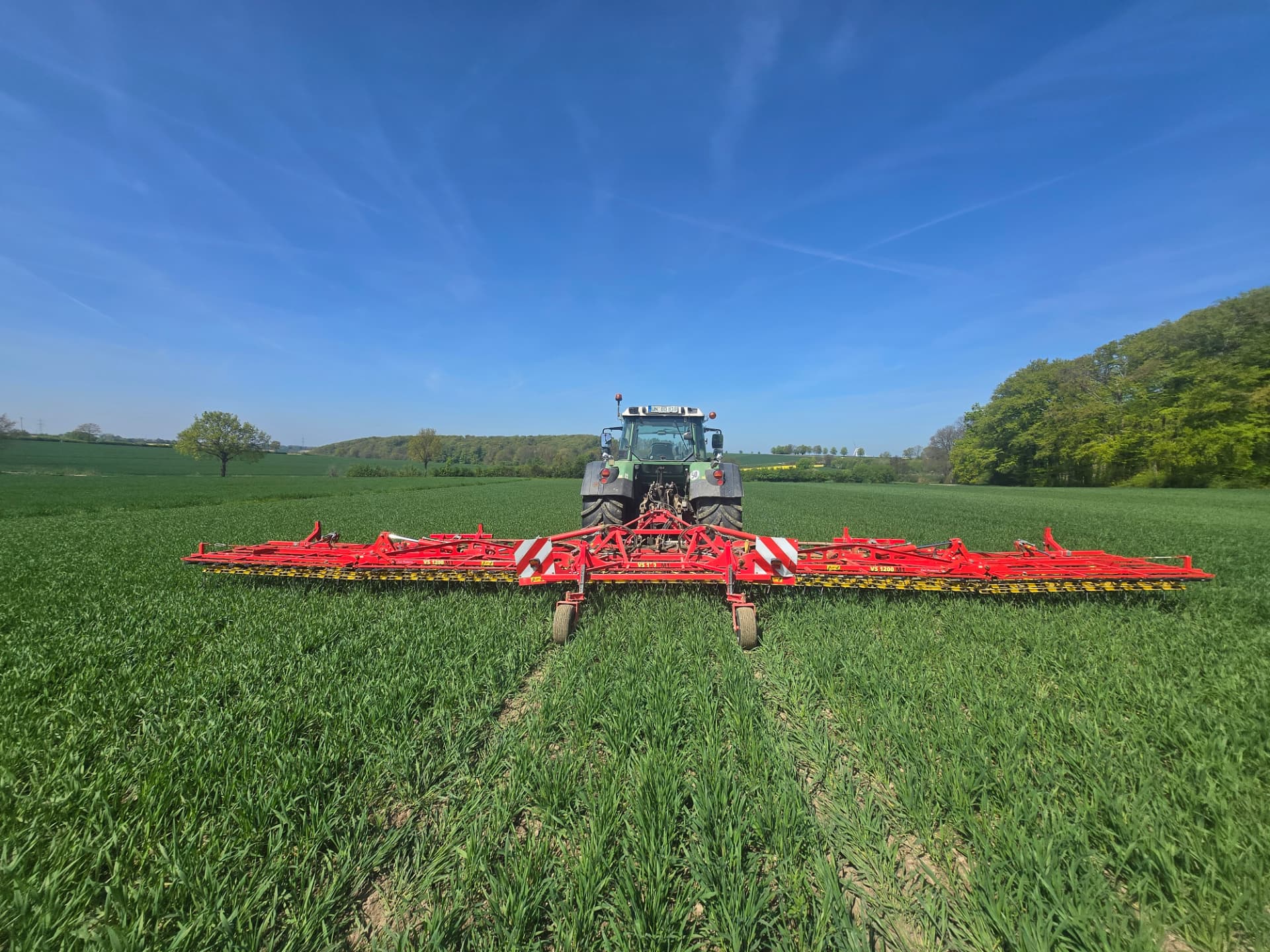 Traktor mit Striegel im grünen Getreidebestand
