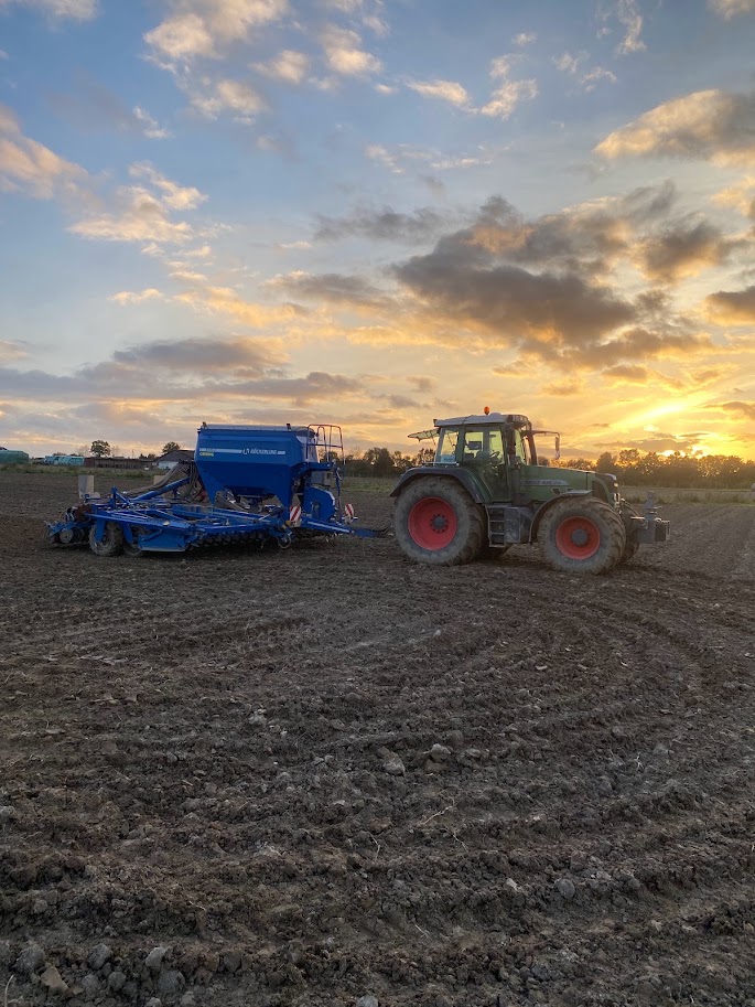 Traktor mit Drillmaschine bei der Aussaat im Sonnenuntergang